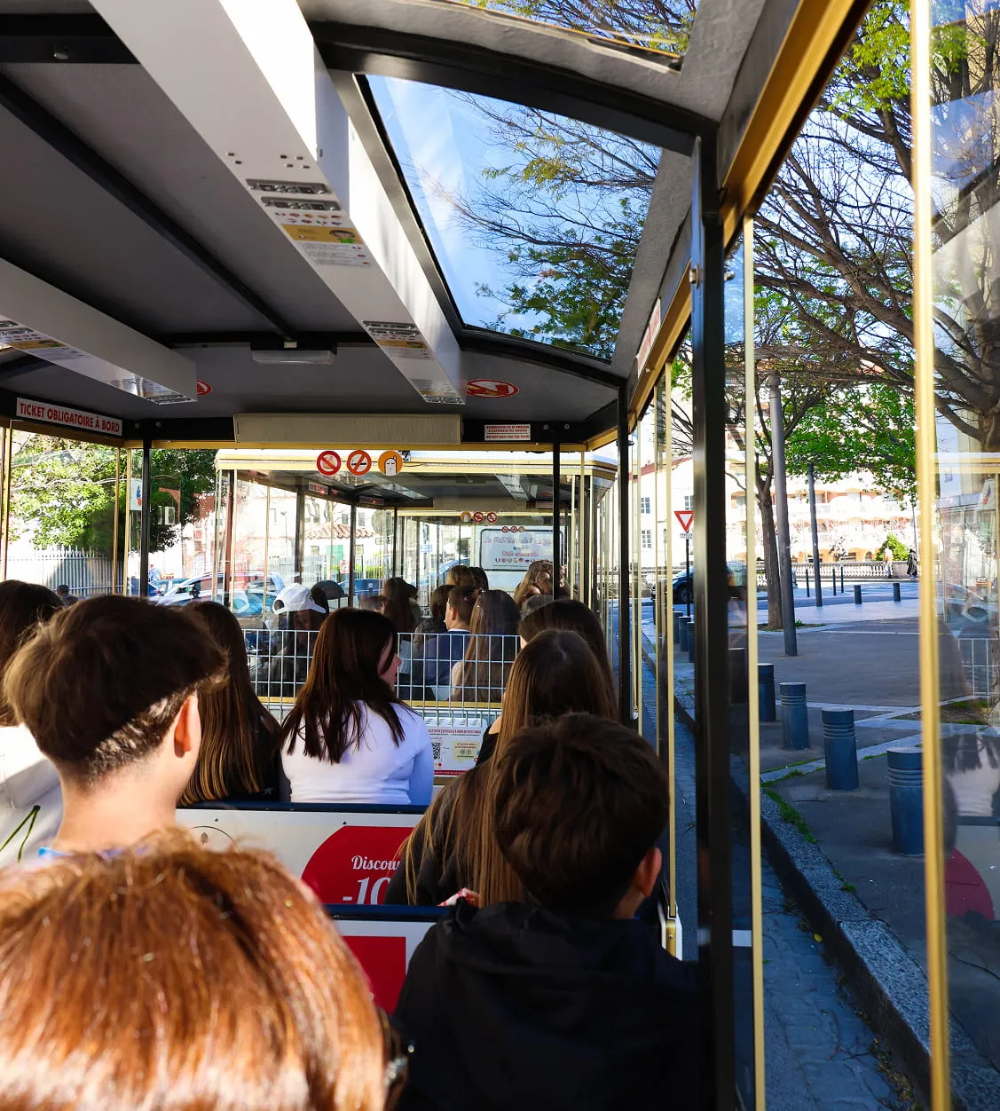 Interior de un tranvía o autobús turístico con varios pasajeros sentados, visto de atrás hacia adelante.