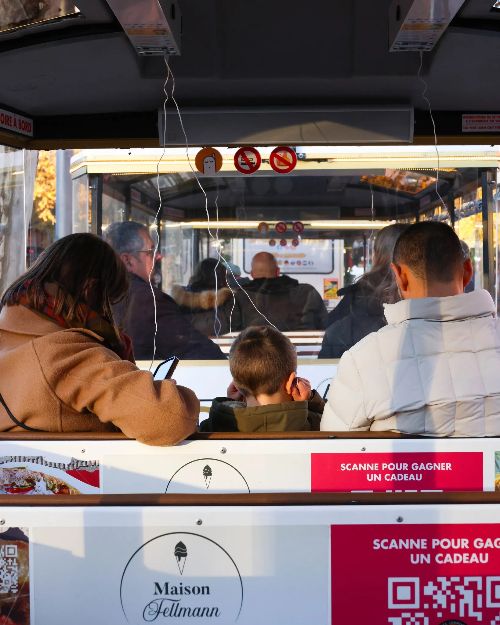 Pasajeros sentados de espaldas en un tranvía, con publicidad de Maison Fellmann en los asientos.